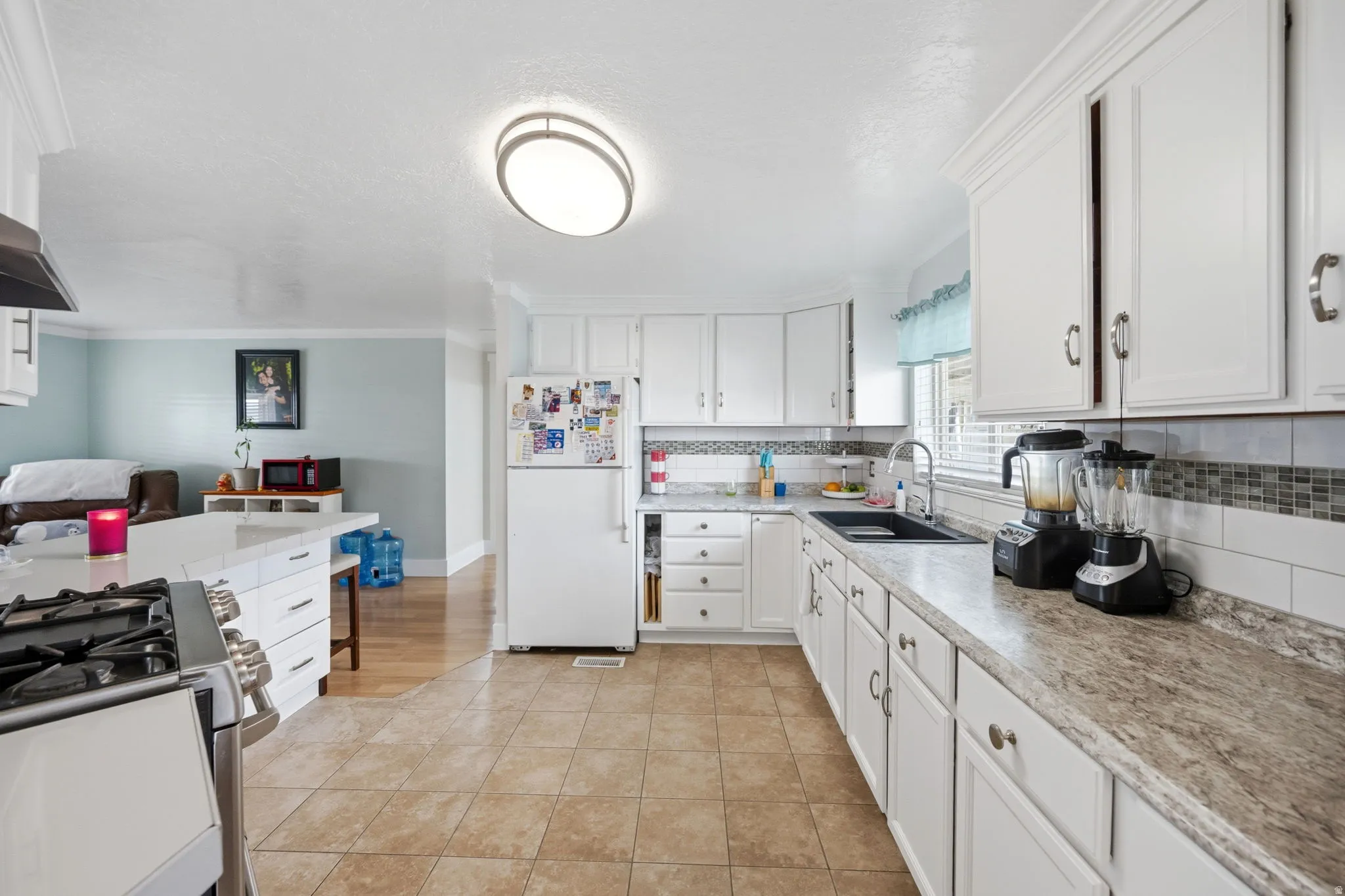 Kitchen with white cabinets, freestanding refrigerator, stainless steel range with gas stovetop, light countertops, and ornamental molding