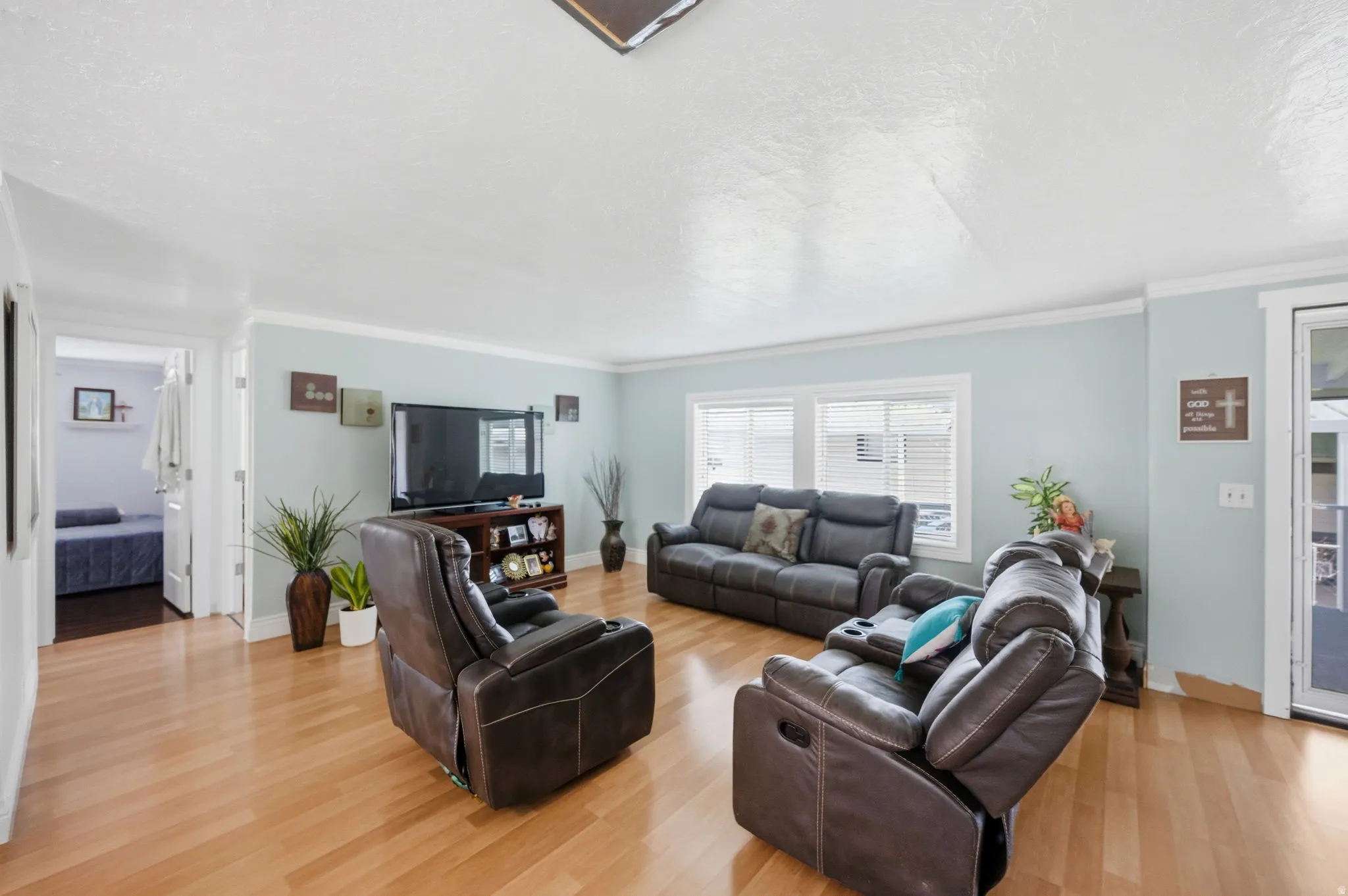 Living area with a textured ceiling, light wood finished floors, and ornamental molding