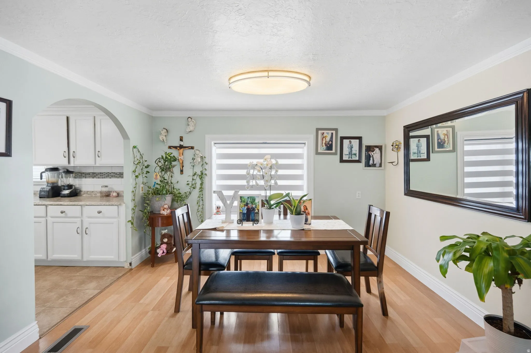 Dining space featuring crown molding, light wood-style flooring, arched walkways, and a textured ceiling