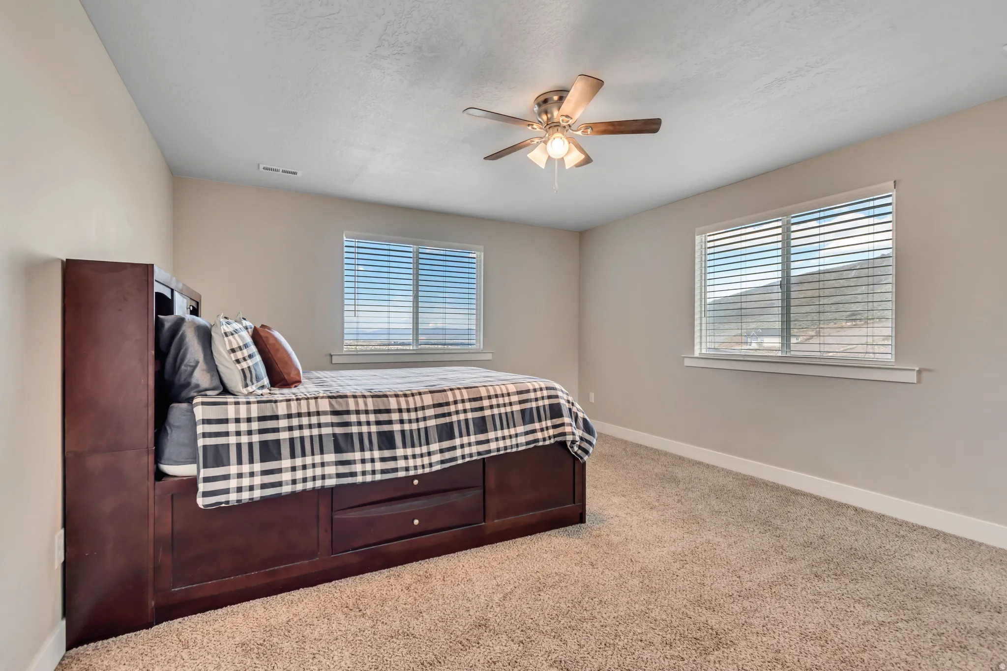 Bedroom featuring light colored carpet, multiple windows, and a ceiling fan