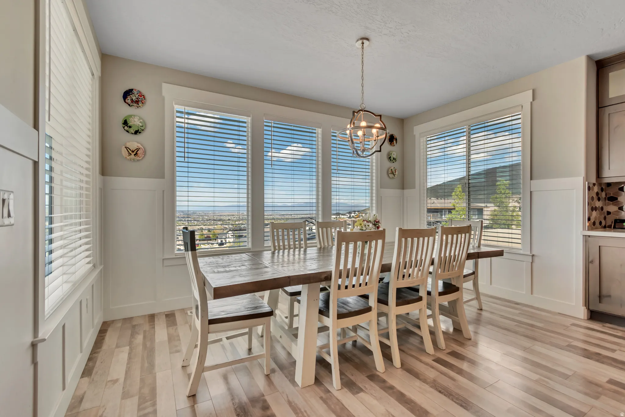 Dining space with a wainscoted wall, light wood-style floors, a decorative wall, and suspended lighting
