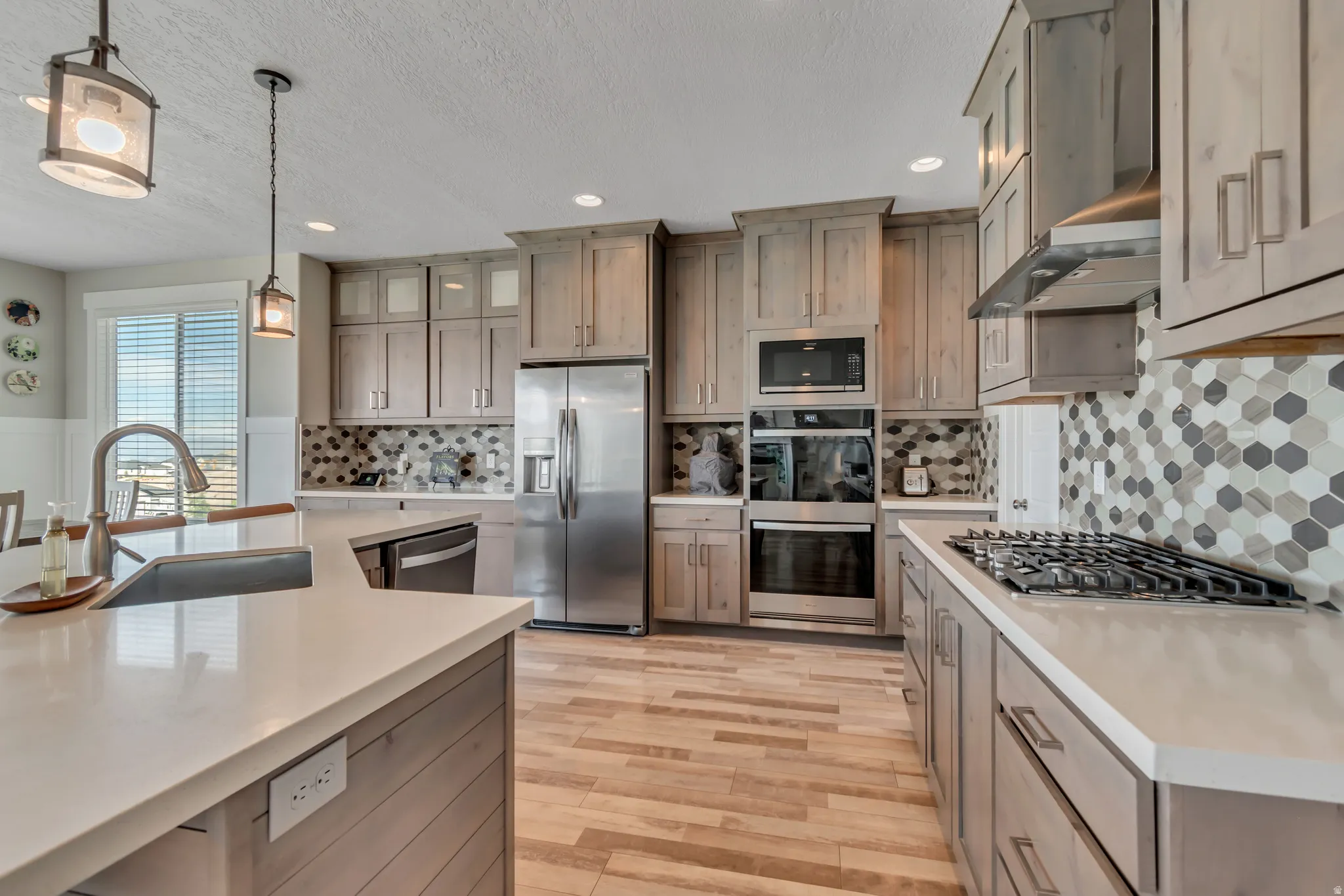 Kitchen with stainless steel appliances, pendant lighting, light wood-style floors, light stone counters, and glass insert cabinets