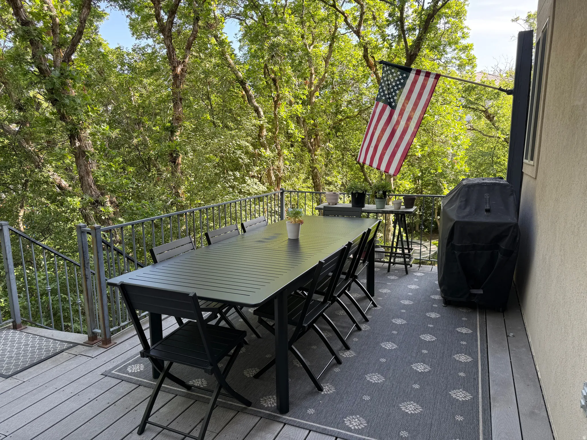 Spacious exterior deck with composite flooring and metal railings, surrounded by mature trees