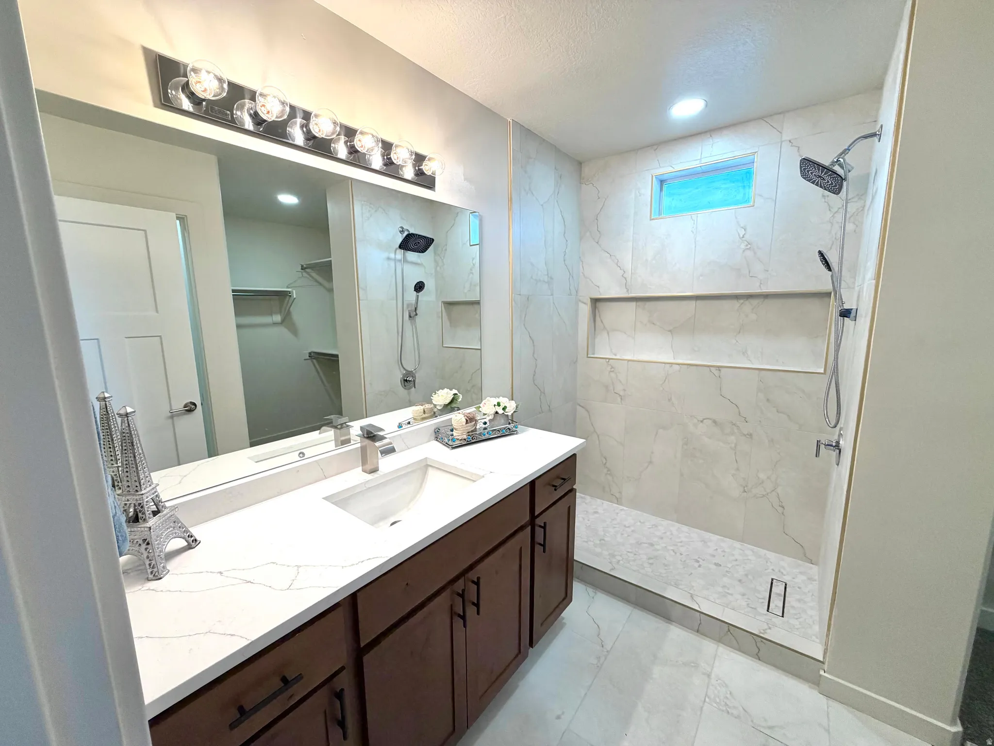 Full bath featuring a marble finish shower, vanity, a walk in closet, light marble finish floors, and recessed lighting