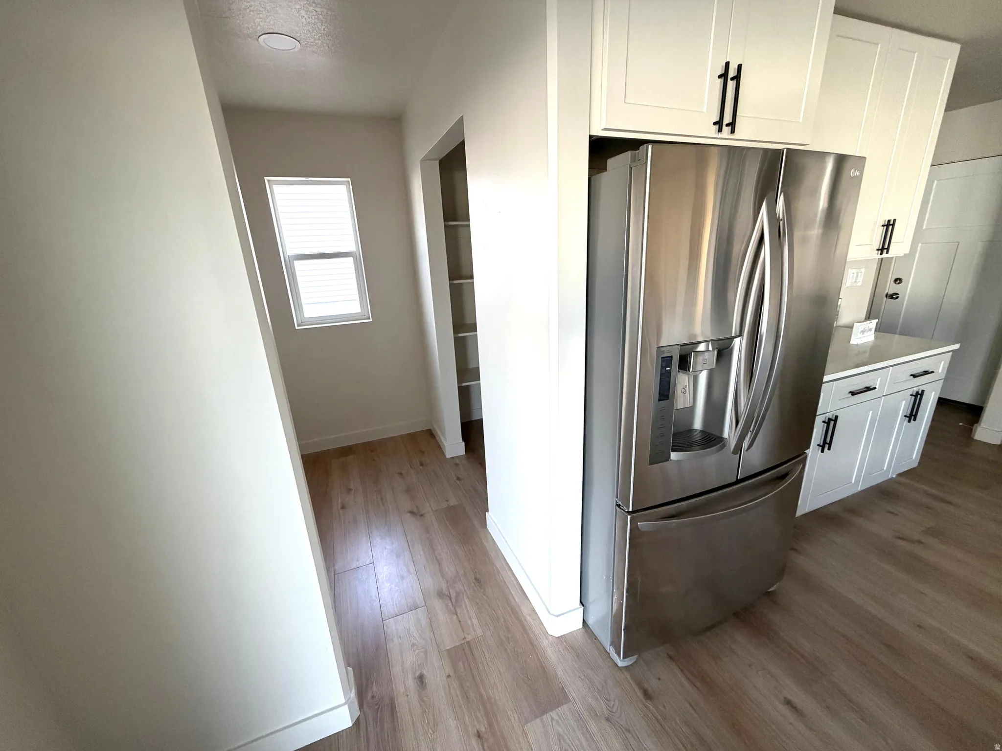 Kitchen featuring stainless steel fridge with ice dispenser, white cabinetry, and light wood-style floors