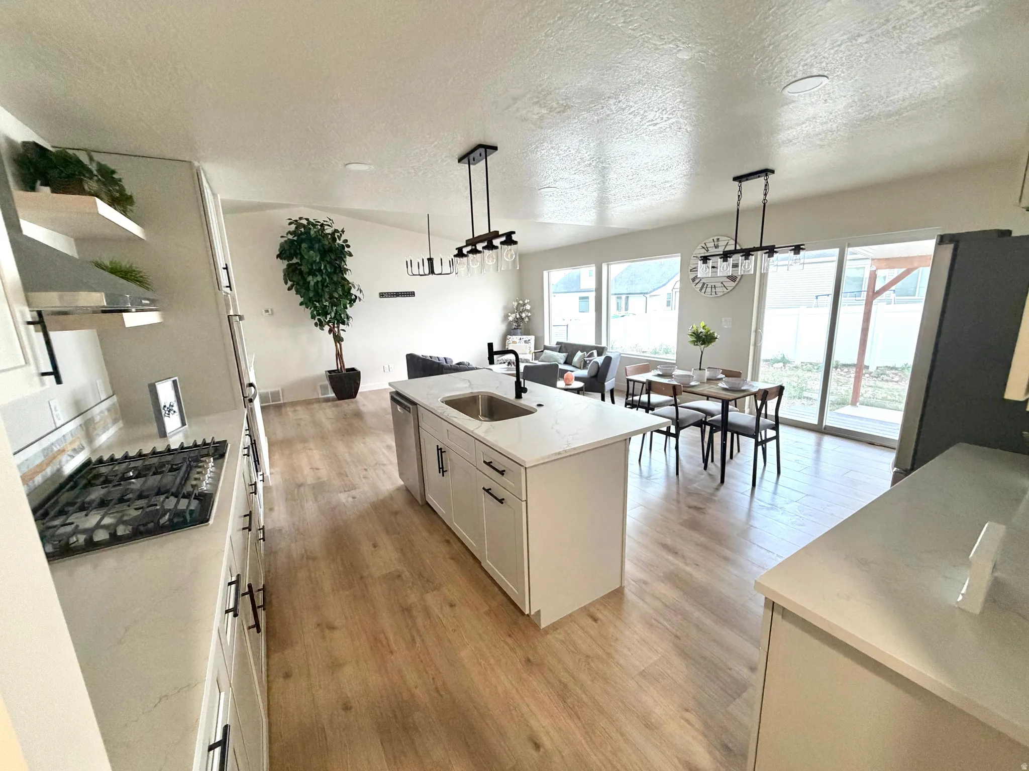 Kitchen featuring decorative light fixtures, stainless steel appliances, an island with sink, light stone countertops, and a textured ceiling
