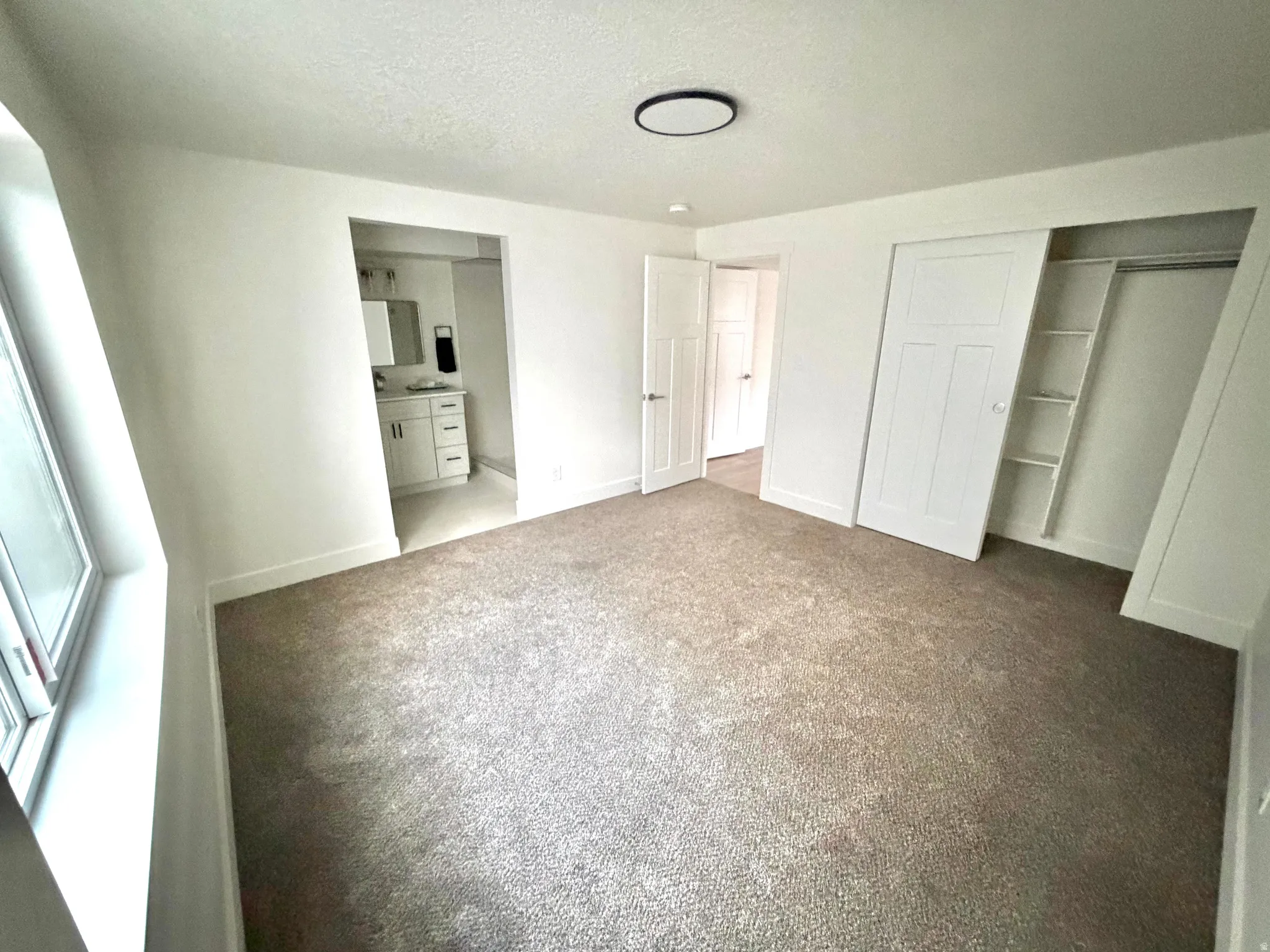 Unfurnished bedroom with light carpet, a closet, a textured ceiling, and ensuite bath