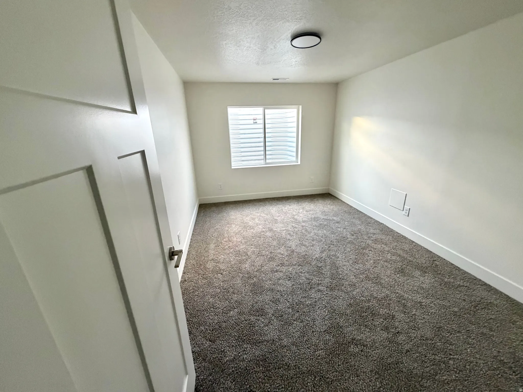 Carpeted spare room featuring a textured ceiling and baseboards