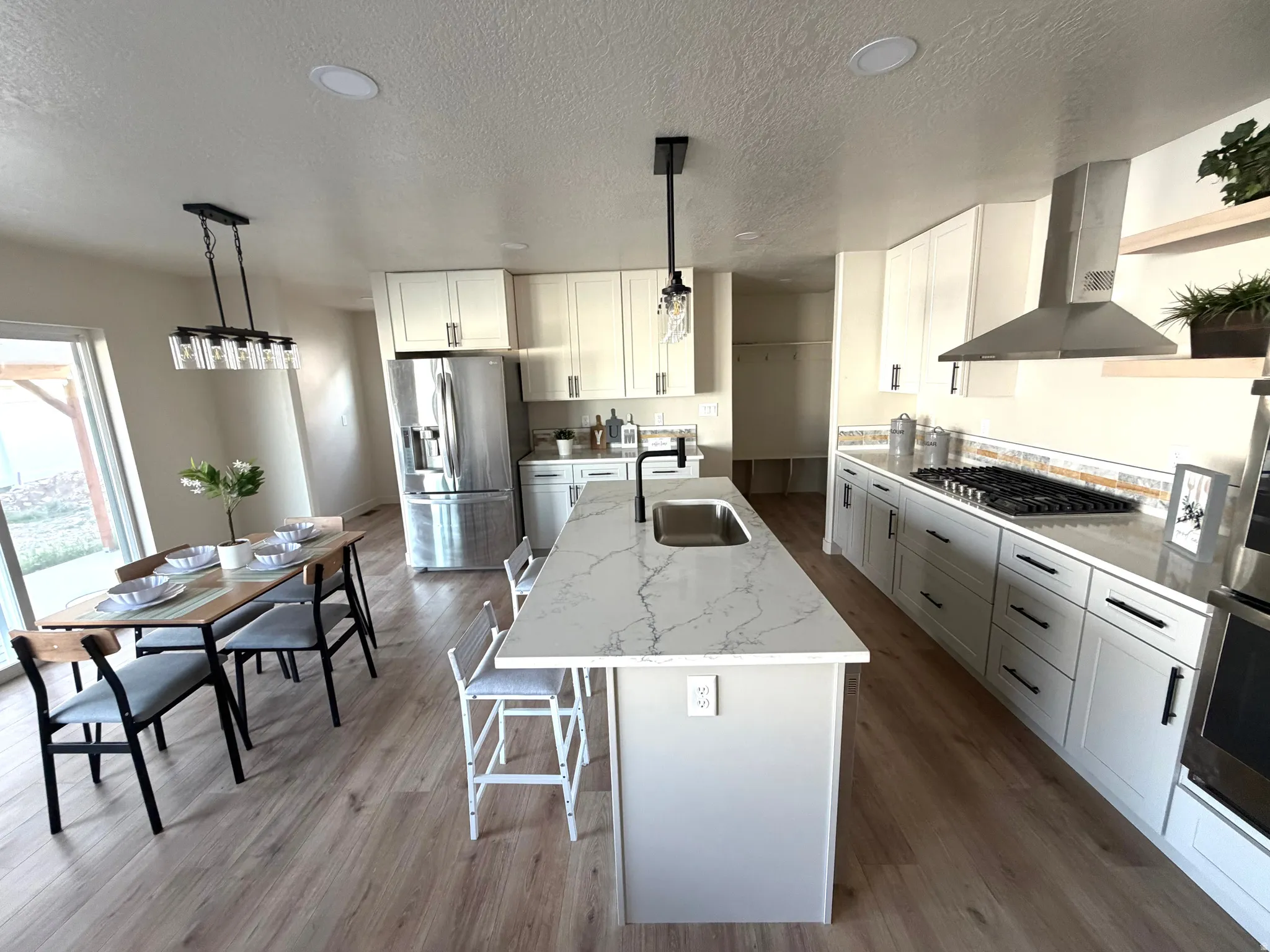 Kitchen with white cabinetry, stainless steel appliances, light stone countertops, a kitchen island with sink, and light wood-style floors