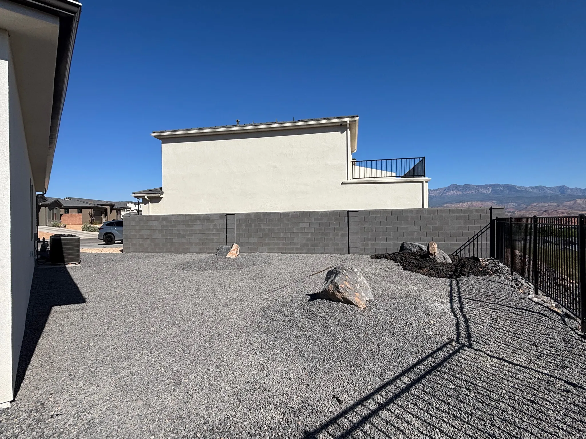 Expansive gravel yard featuring a privacy block wall and a black metal fence