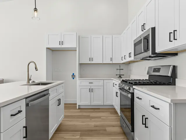 Kitchen with stainless steel appliances, light wood-type flooring, white cabinetry, hanging light fixtures, and light stone countertops