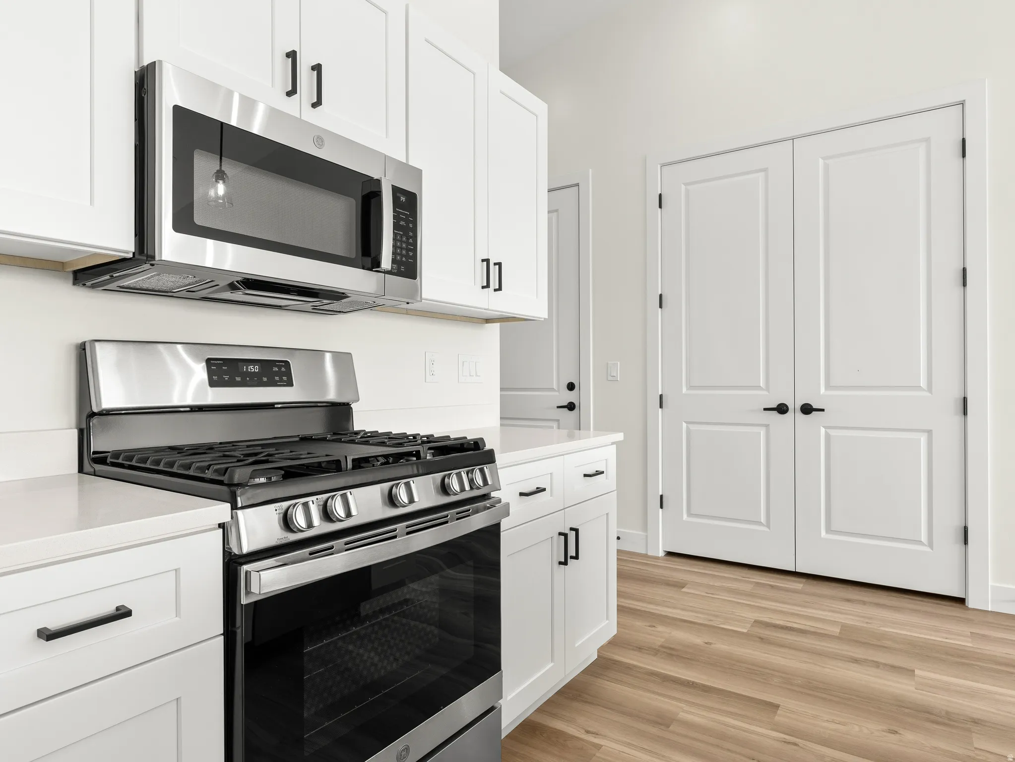 Kitchen with stainless steel appliances, white cabinets, light wood-style floors, and light stone countertops
