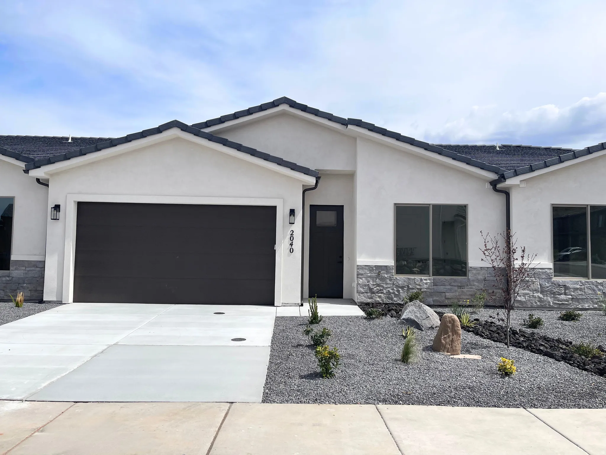 View of front of house with stone siding, a garage, concrete driveway, stucco siding, and a tiled roof