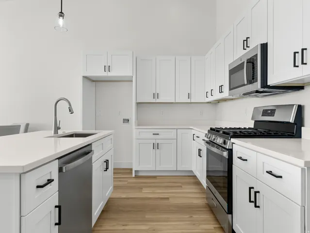 Kitchen featuring stainless steel appliances, white cabinets, light wood finished floors, and a center island with sink