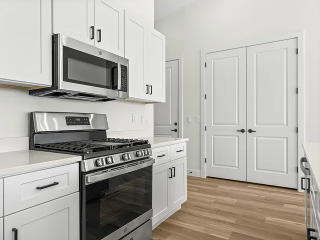 Kitchen featuring stainless steel appliances, white cabinetry, light wood-style floors, and light stone countertops