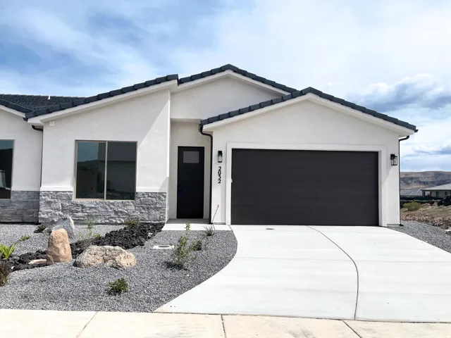 View of front of property with a garage, concrete driveway, stucco siding, and stone siding