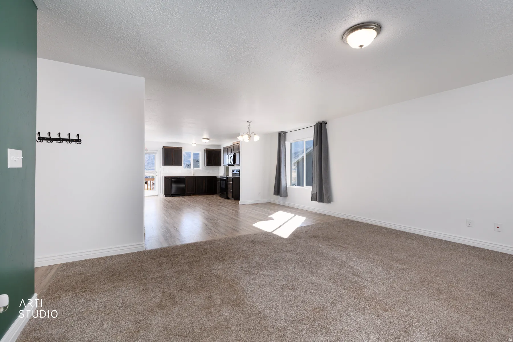 Unfurnished living room featuring hanging lights, light colored carpet, and a textured ceiling