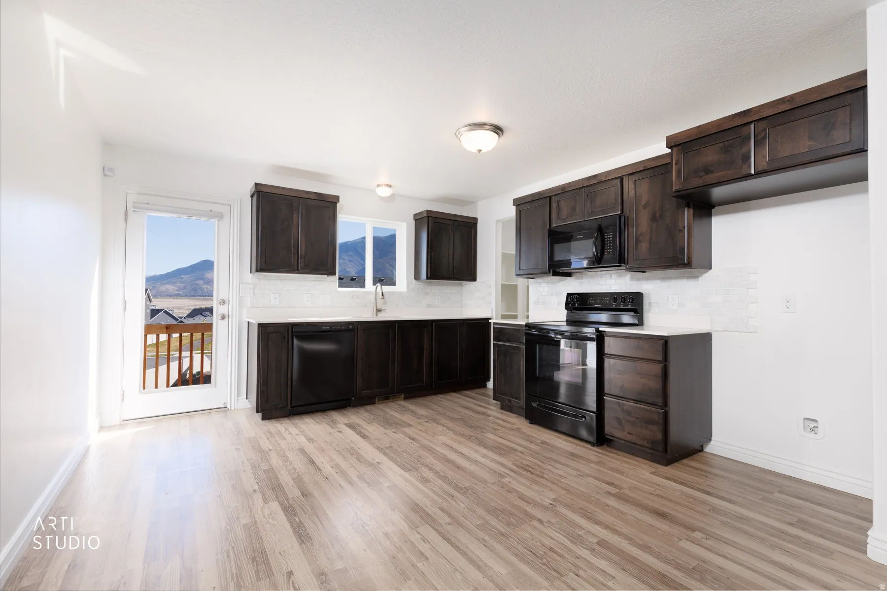 Kitchen featuring dark wood finish cabinets, black appliances, and light quartz countertops