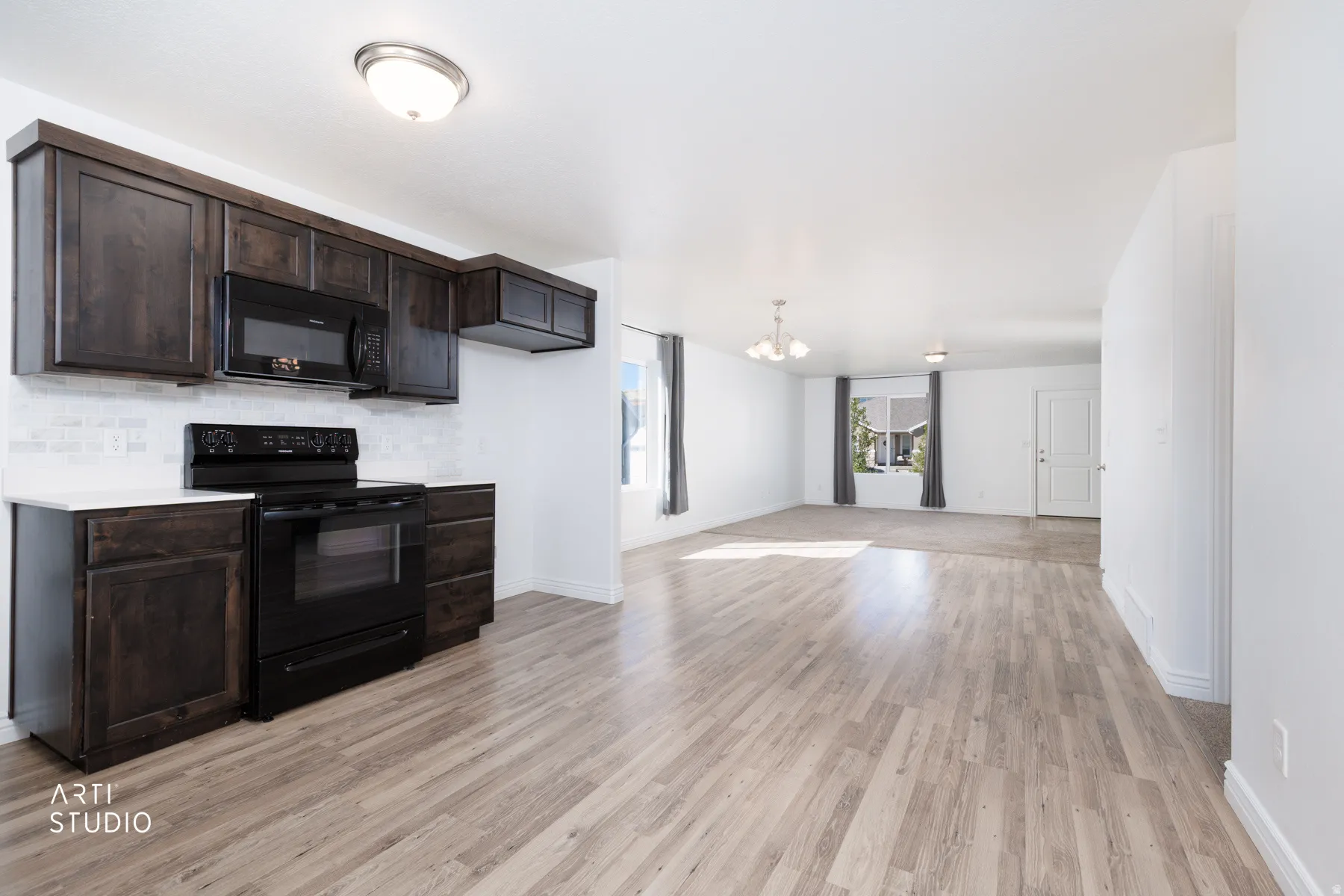 Kitchen featuring dark wood finish cabinetry, black appliances, light quartz countertops, suspended lighting, and decorative backsplash