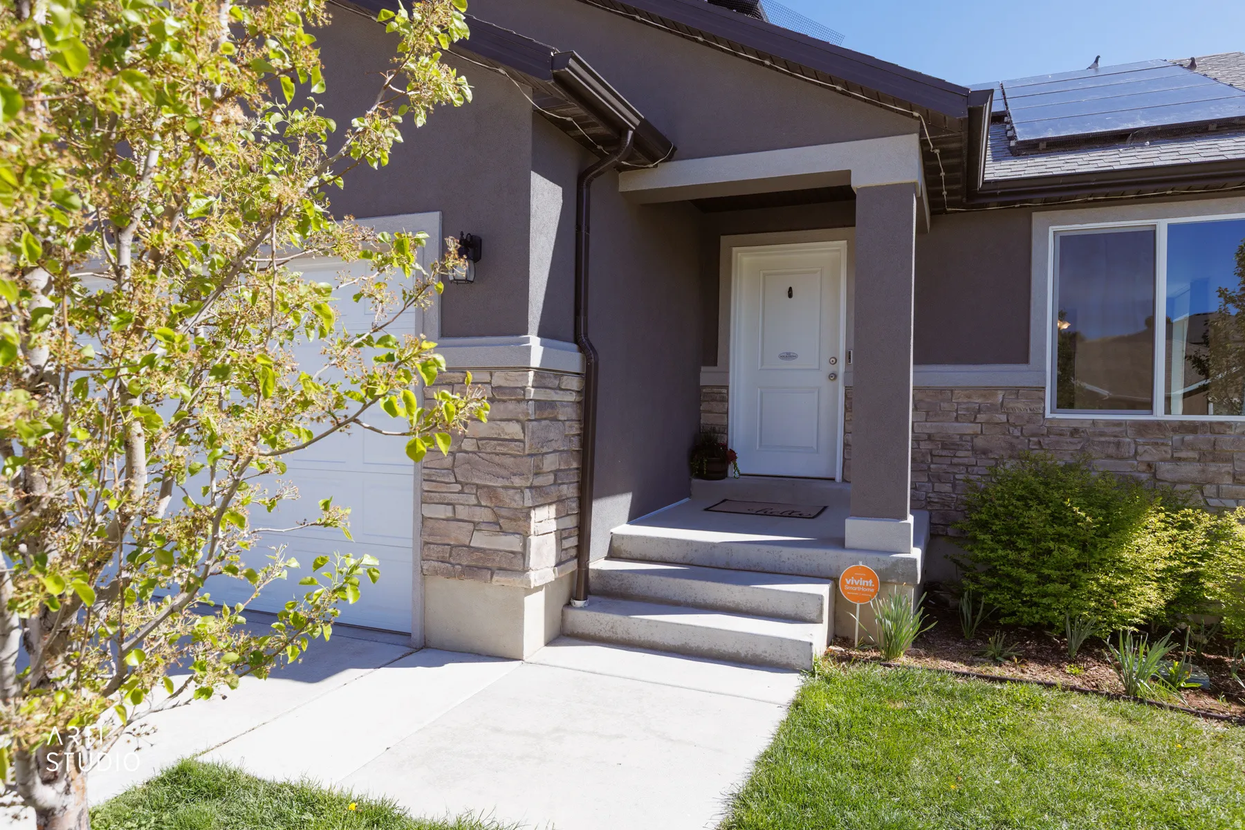 Property entrance with stone siding, roof mounted solar panels, and stucco siding