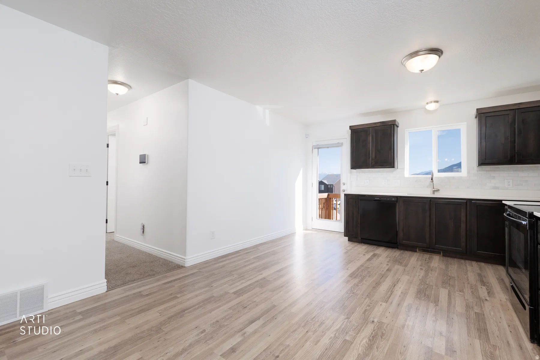 Kitchen with dark wood finish cabinetry, light quartz countertops, black appliances, tasteful backsplash, and light wood-style floors