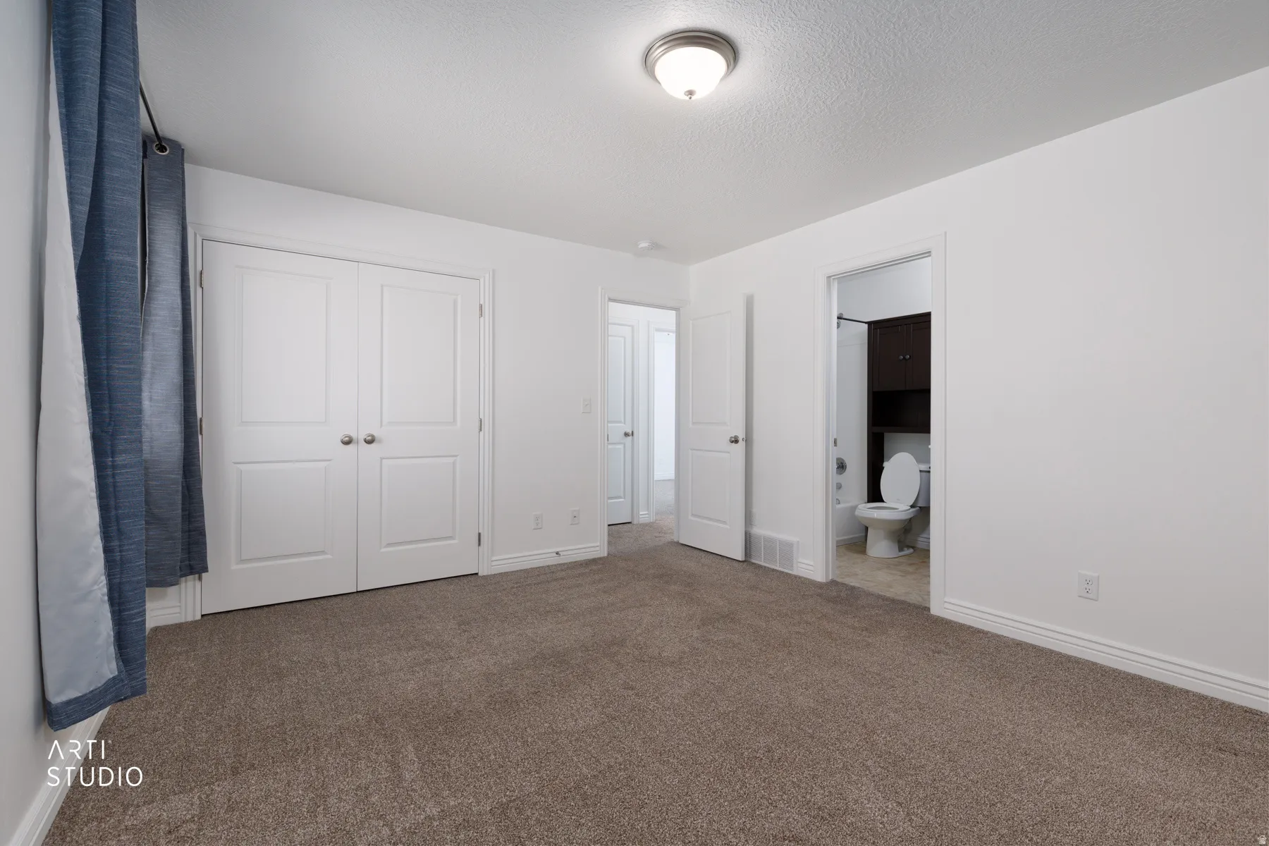 Unfurnished primary bedroom featuring carpet, a closet, ensuite bathroom, and a textured ceiling