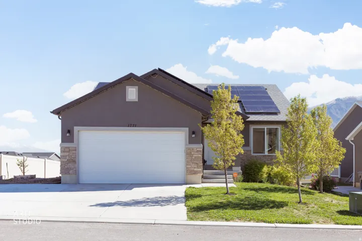 Ranch-style house featuring stone siding, an attached garage, solar panels, concrete driveway, and a front lawn