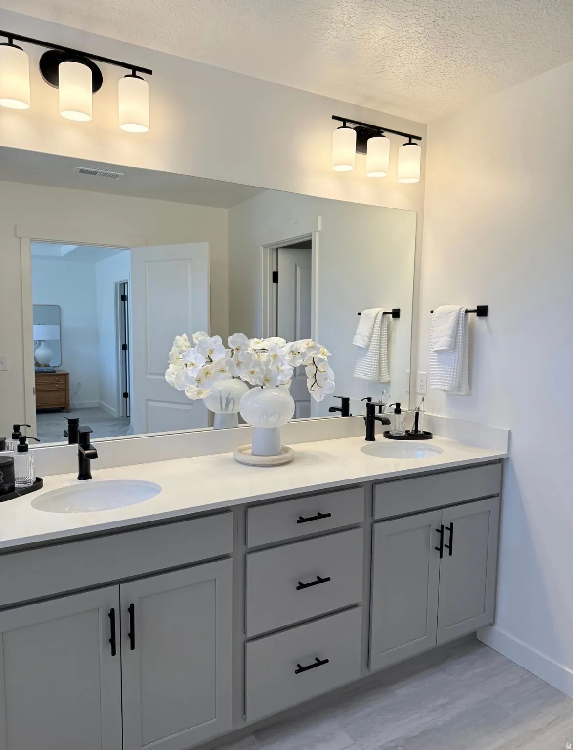 Dual vanity with light gray cabinetry and matte black hardware, featuring undermount sinks and light-toned countertops