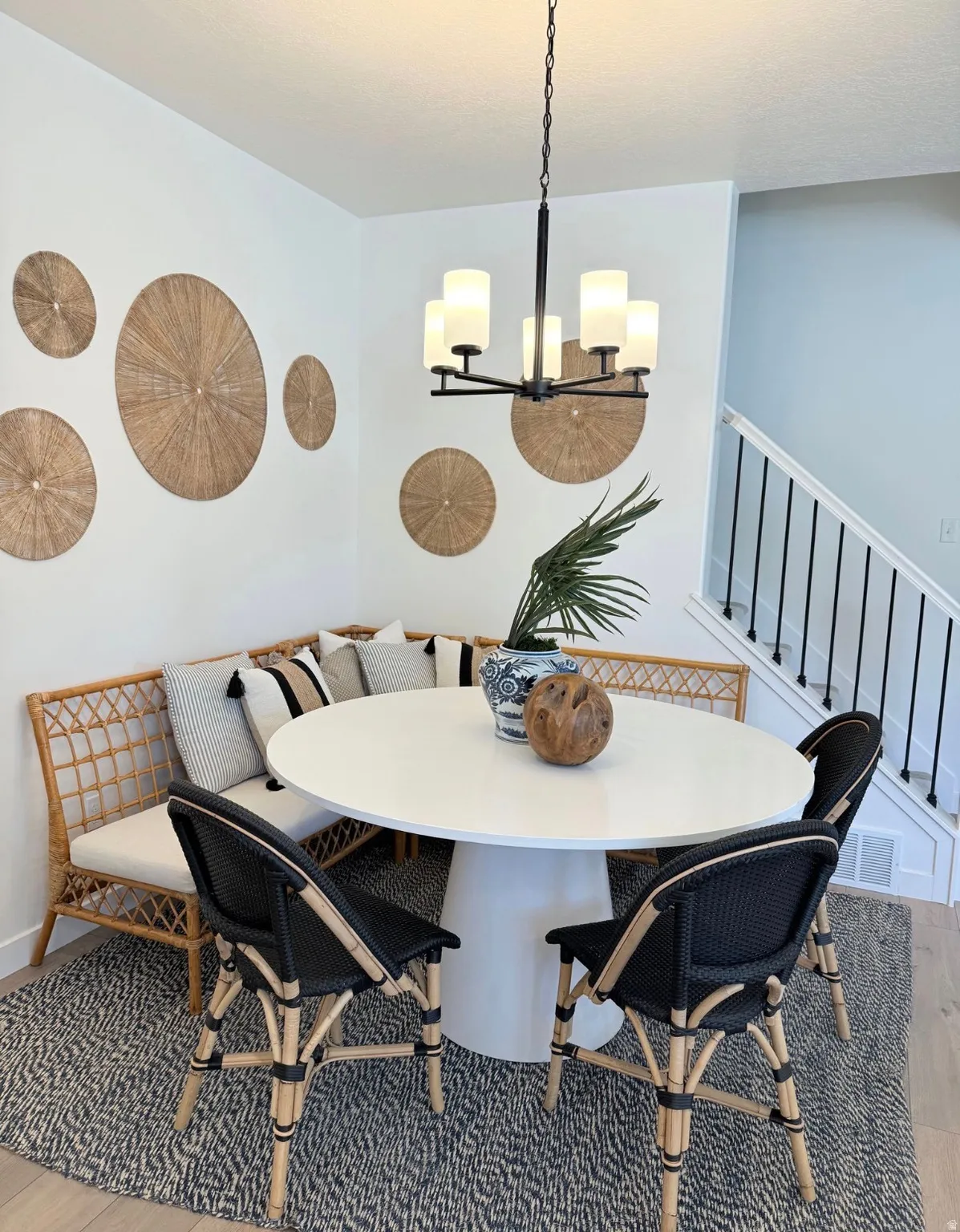 Dining area featuring a contemporary white round table with a pedestal base, a black metal chandelier with five frosted glass shades, and light wood-finish flooring