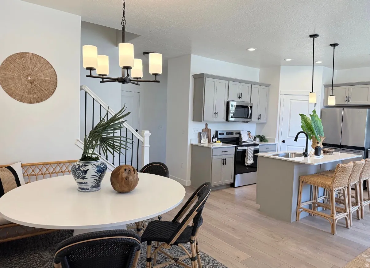 Open-concept living space featuring wood-finish flooring, a contemporary kitchen with light gray cabinetry, stainless steel appliances, and a central island with bar seating