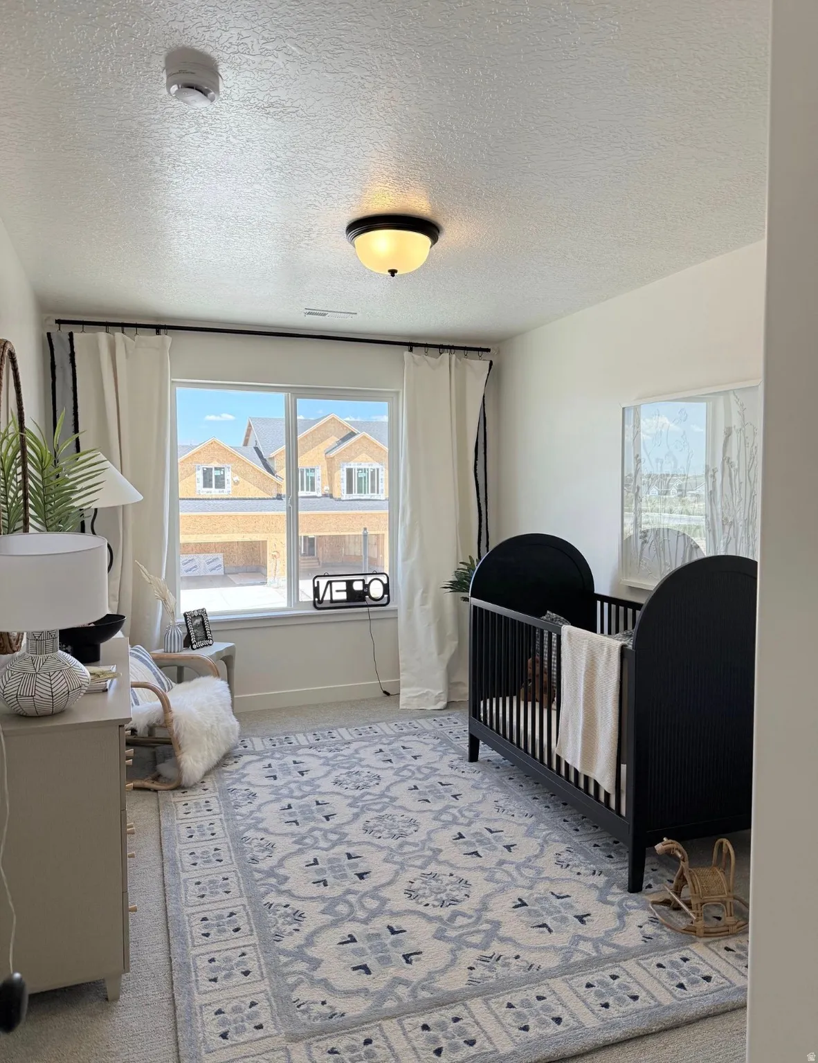 Bright room featuring a large window with white window treatments, a central ceiling light fixture, and textured carpeting