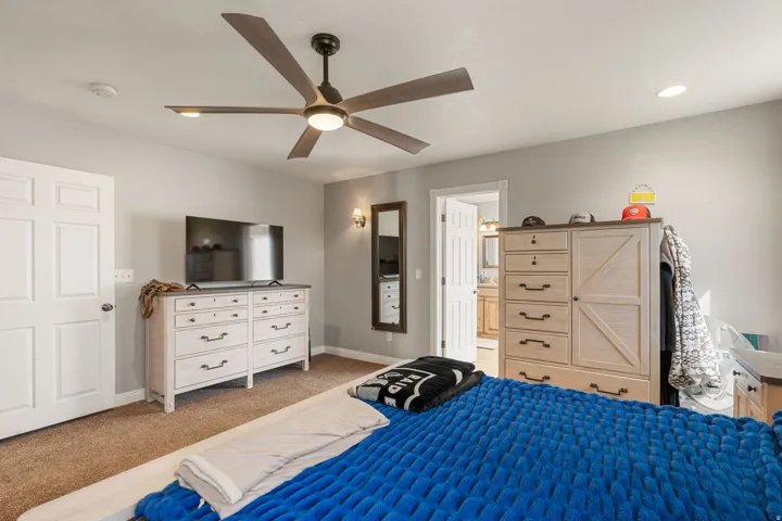 Primary bedroom featuring a ceiling fan, light colored carpet, and ensuite bathroom