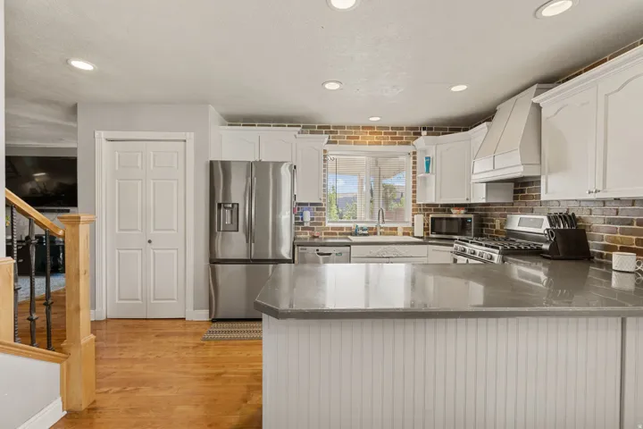 Kitchen with stainless steel appliances, a peninsula, white cabinets, dark  counters, and light wood-style floors