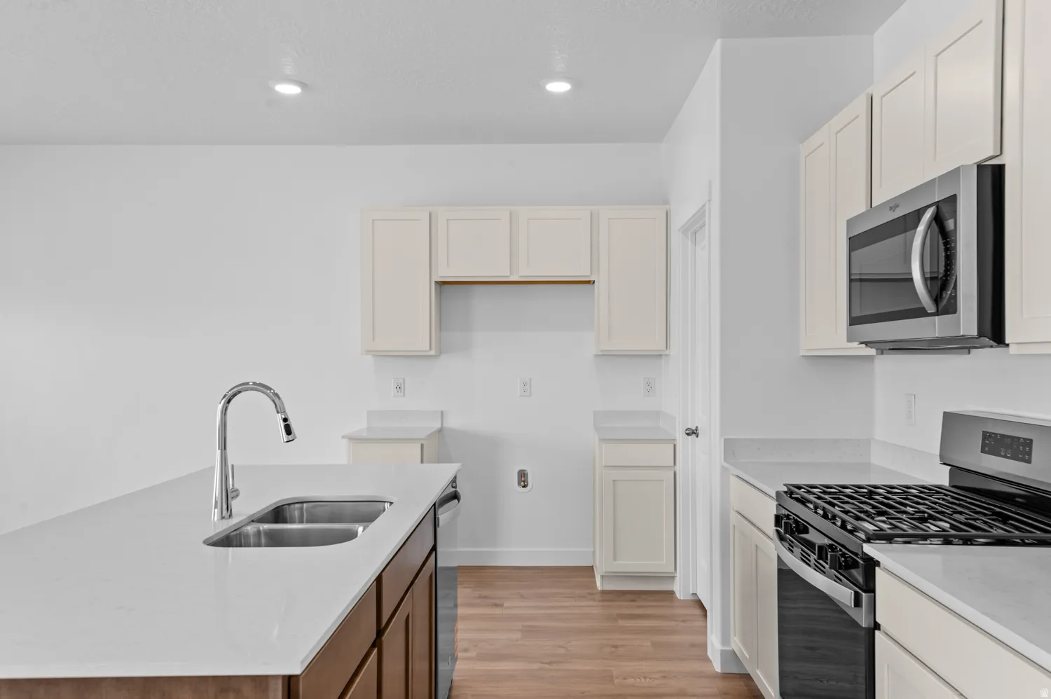 Kitchen with stainless steel appliances, an island with sink, light stone countertops, light wood-style flooring, and two tone color scheme