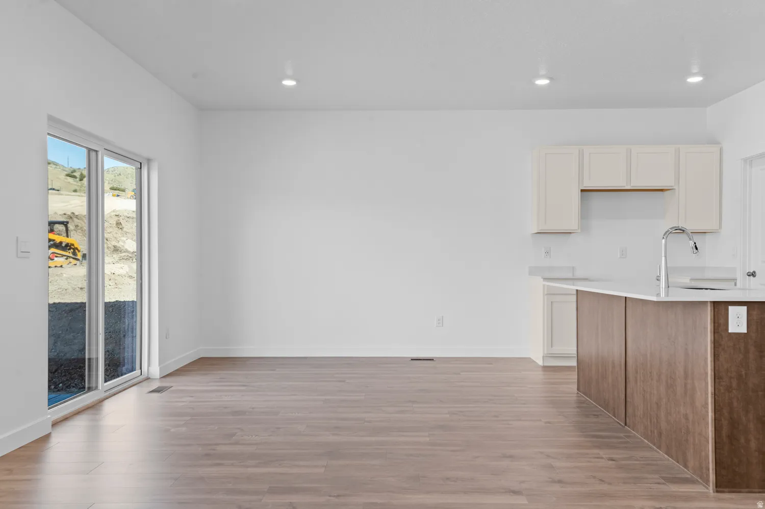Kitchen featuring dual tone cabinets, light wood-type flooring, light stone counters, a kitchen island with sink, and recessed lighting