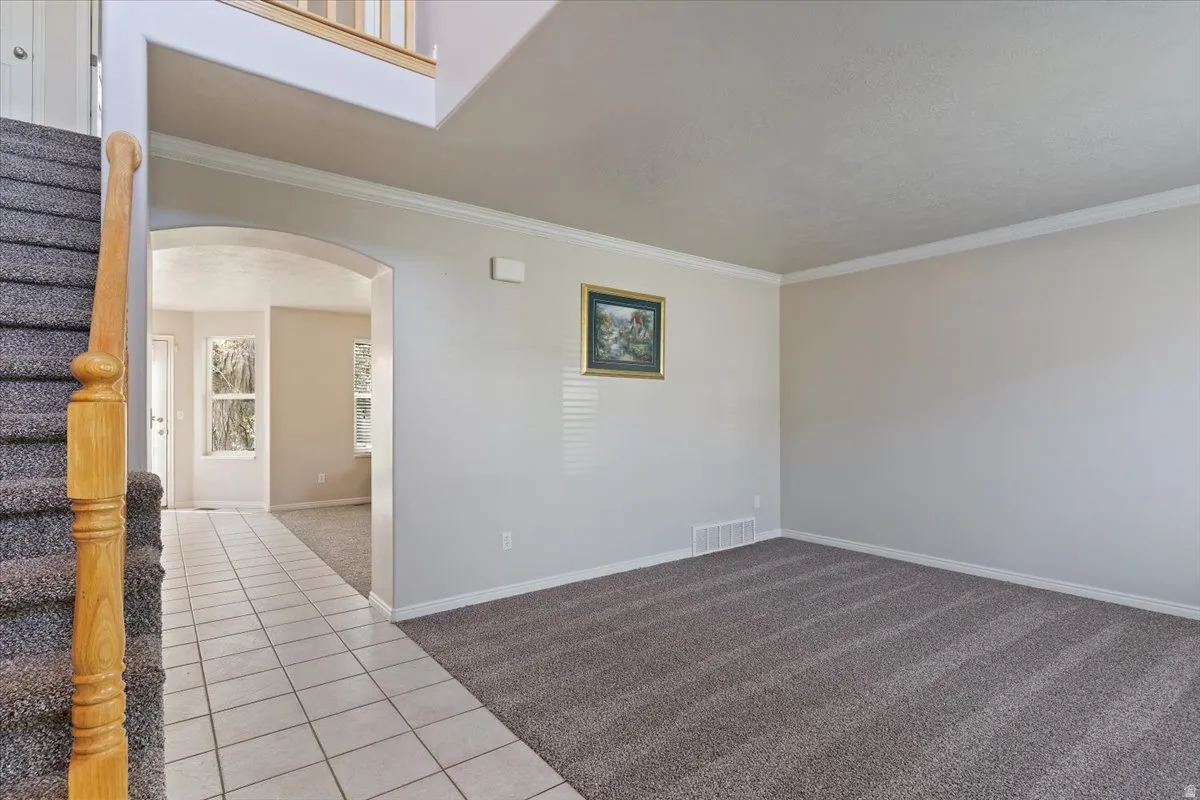 Unfurnished room featuring arched walkways, light tile patterned floors, light carpet, and ornamental molding
