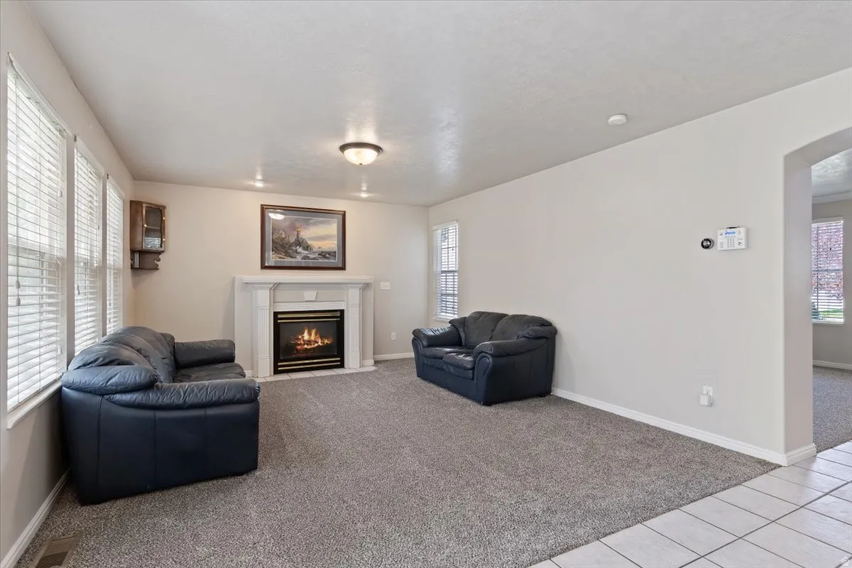 Living room featuring light carpet, arched walkways, a fireplace with flush hearth, and light tile patterned floors
