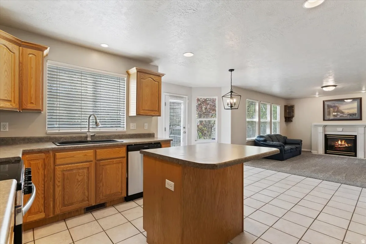 Kitchen featuring light tile patterned flooring, a kitchen island, open floor plan, a warm lit fireplace, and a textured ceiling
