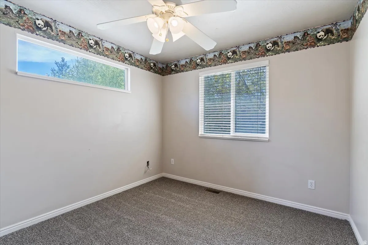 Empty room featuring ceiling fan, dark colored carpet, and healthy amount of natural light