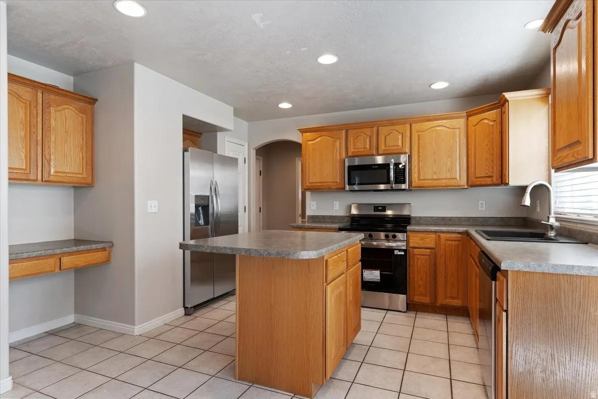 Kitchen with stainless steel appliances, arched walkways, a kitchen island, light tile patterned flooring, and wood finish cabinets