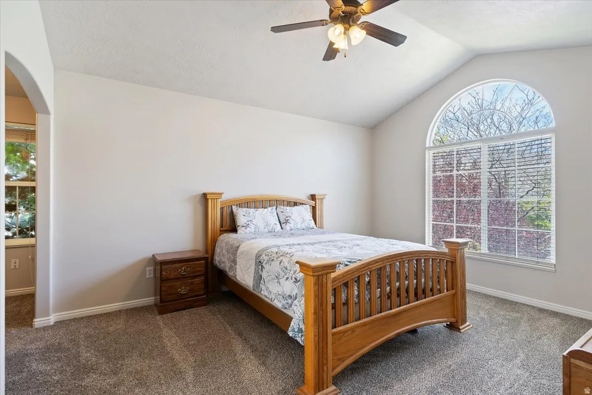 Bedroom featuring lofted ceiling, dark colored carpet, ceiling fan, and arched walkways