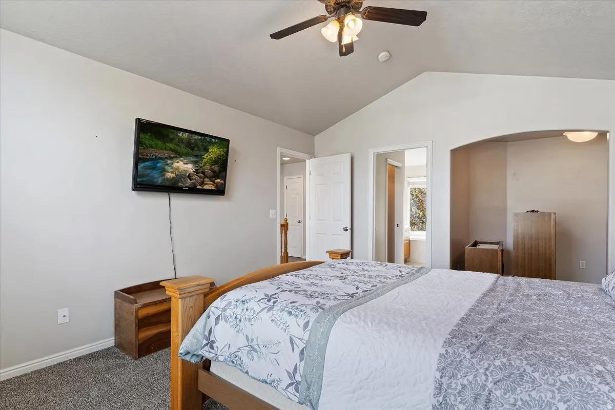 Carpeted bedroom with a ceiling fan, ensuite bath, and arched walkways
