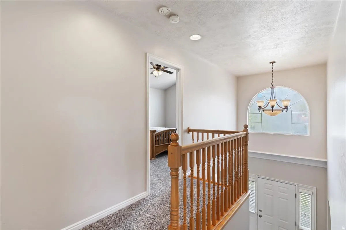 Hallway with carpet, an upstairs landing, plenty of natural light, suspended lighting, and a textured ceiling