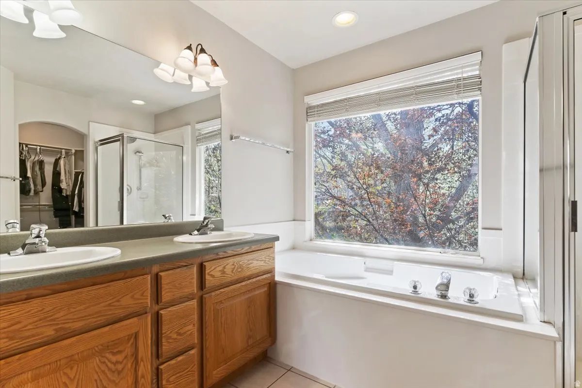 Full bath with a walk in closet, a garden tub, double vanity, a stall shower, and light tile patterned flooring