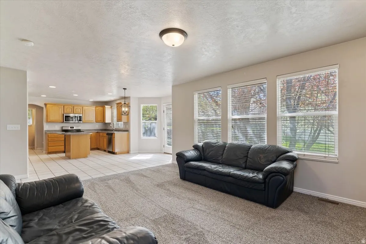 Living room with light colored carpet, a textured ceiling, recessed lighting, light tile patterned flooring, and arched walkways