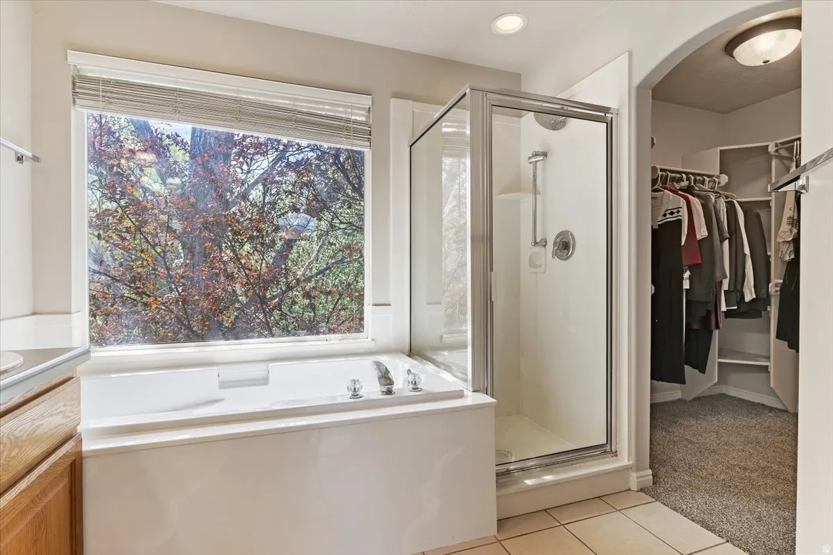 Full bathroom with light colored carpet, a shower stall, a spacious closet, a garden tub, and light tile patterned floors