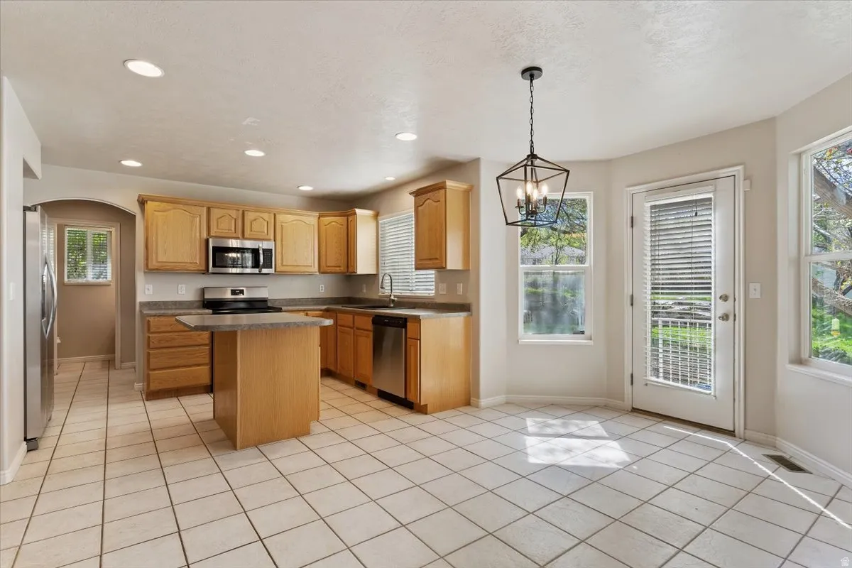 Kitchen with dark countertops, stainless steel appliances, arched walkways, a kitchen island, and a chandelier