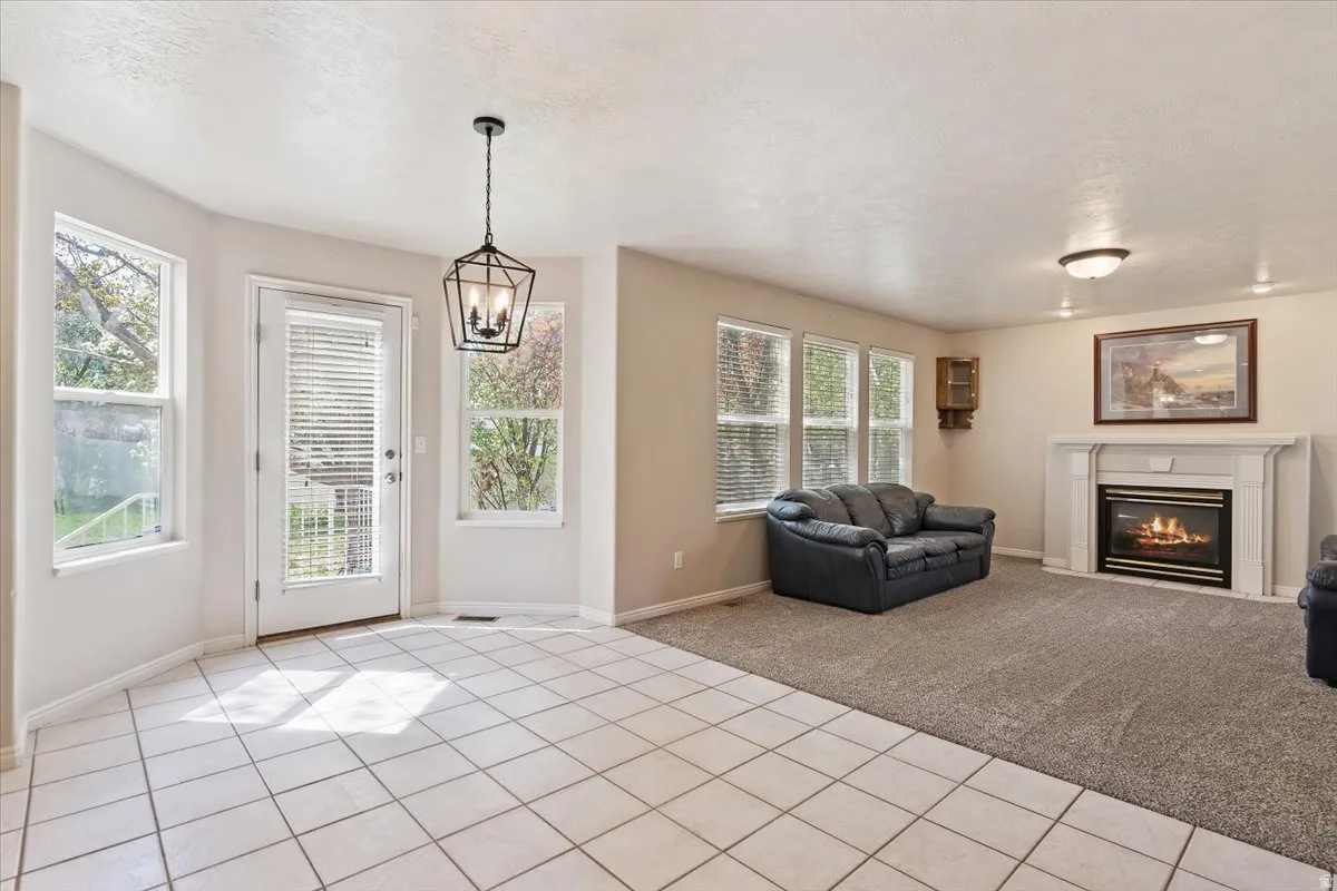 Living room featuring a glass covered fireplace, light tile patterned floors, light colored carpet, a textured ceiling, and suspended lighting