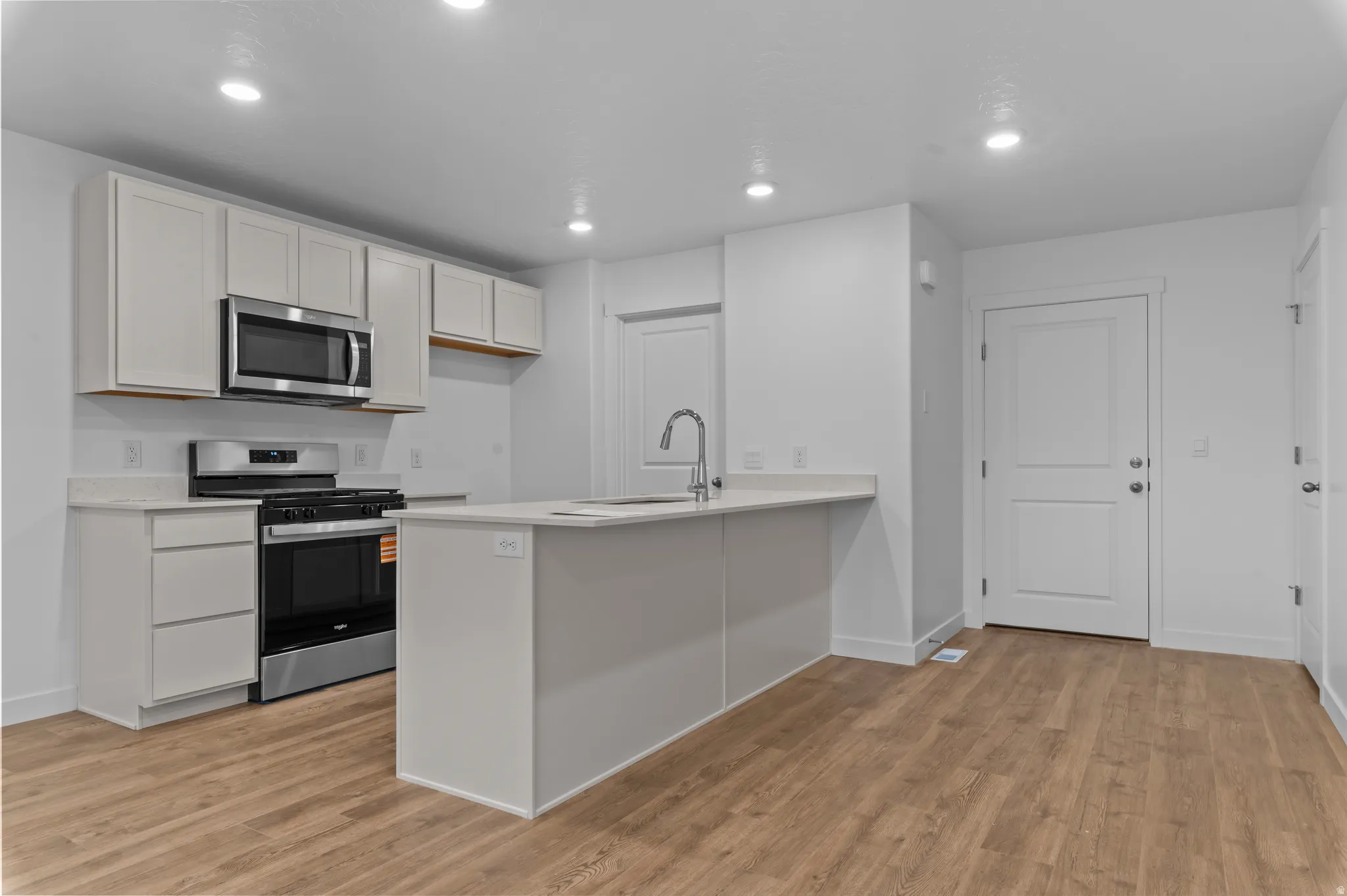 Kitchen featuring stainless steel appliances, a peninsula, light wood finished floors, recessed lighting, and white cabinets
