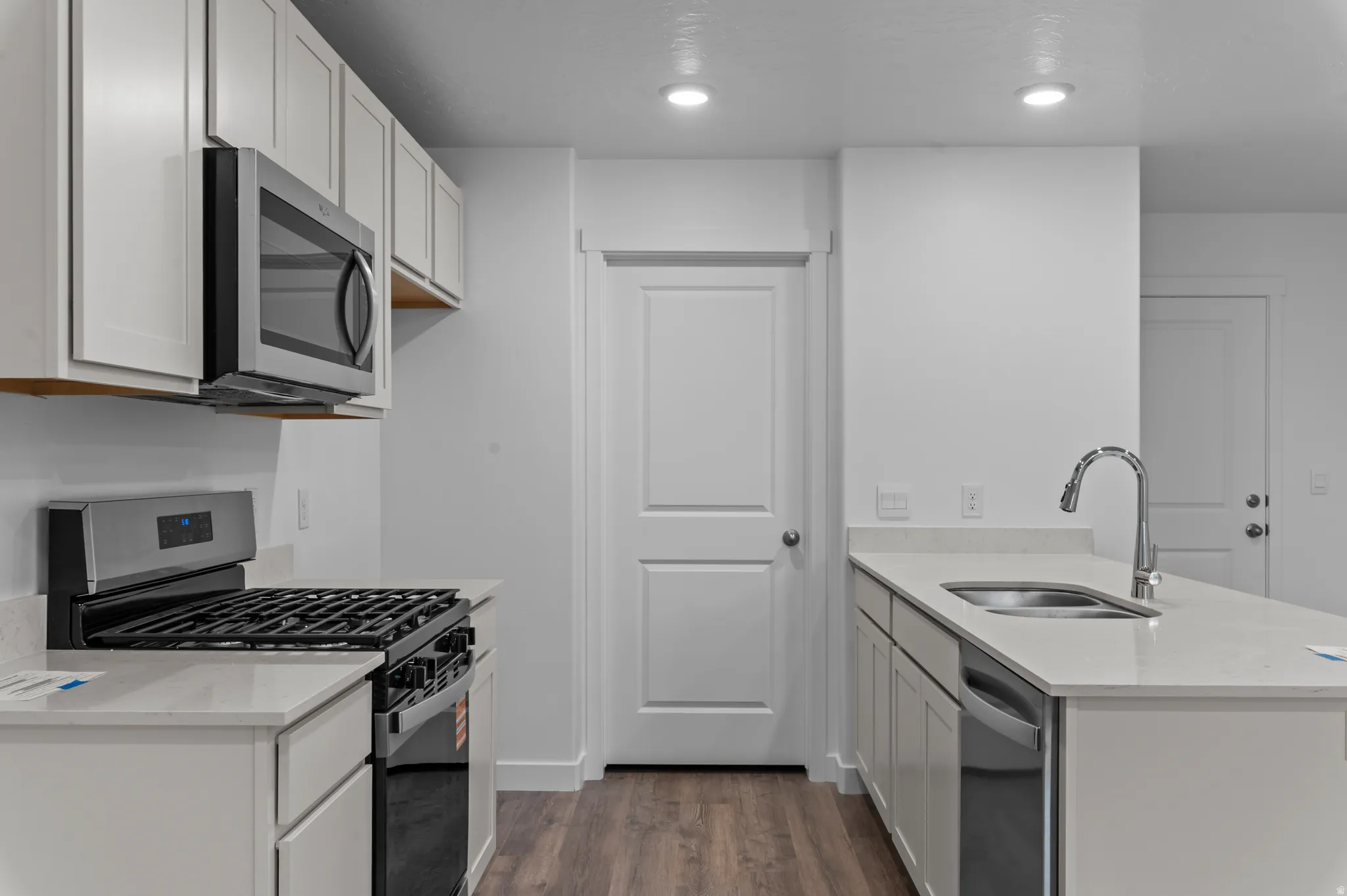 Kitchen with stainless steel appliances, a peninsula, light stone counters, dark wood-type flooring, and recessed lighting
